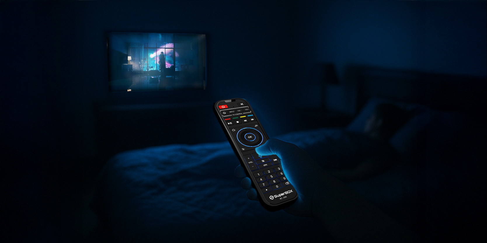 Backlit SuperBox remote being used in a dark bedroom entertainment setup